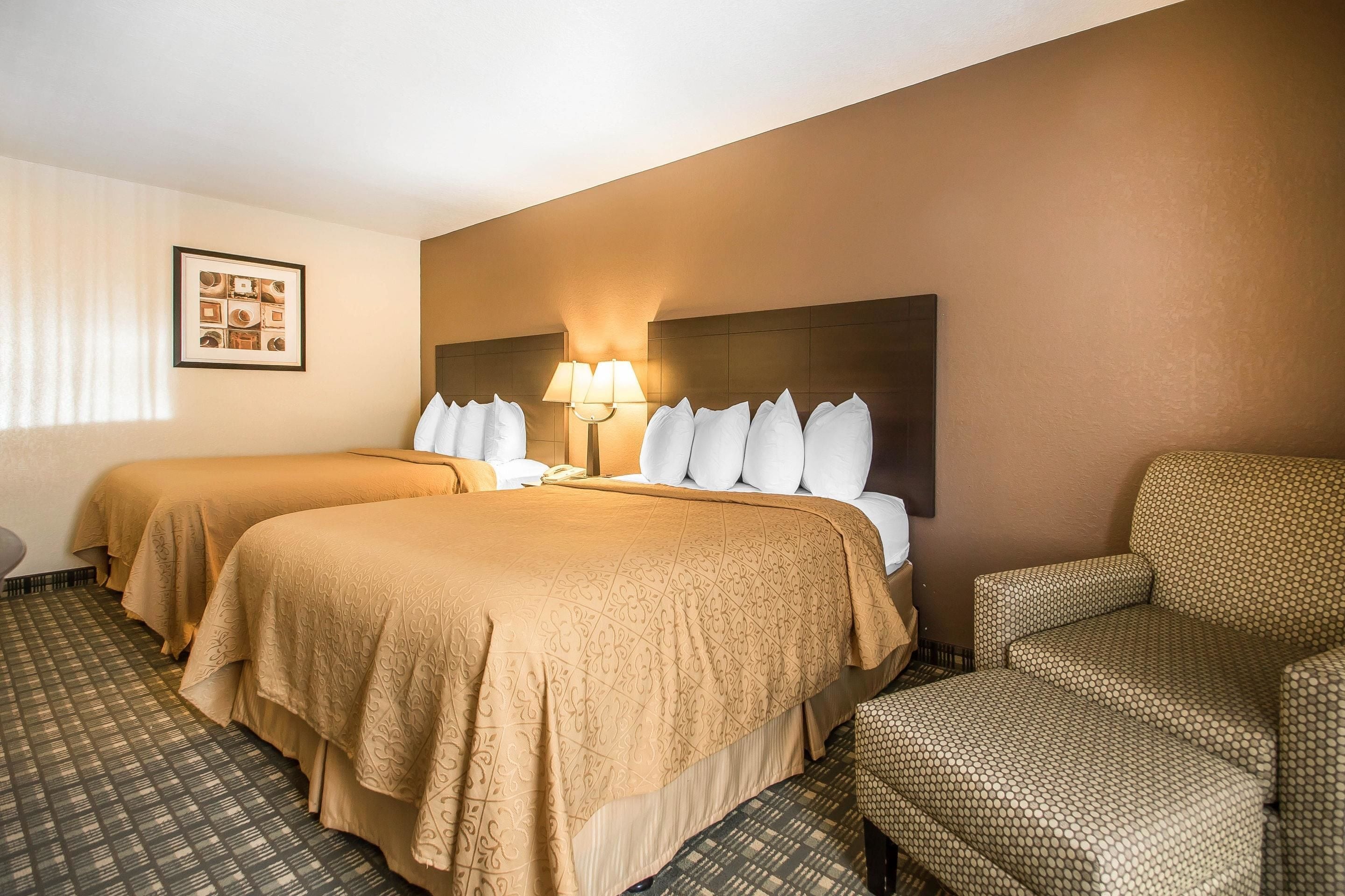 A hotel room with two beds, a sofa, a lamp, and a framed picture on the wall.