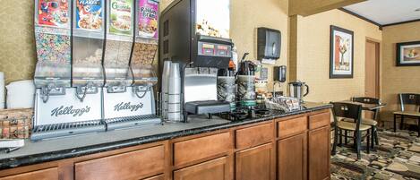 A hotel kitchen with a self-serve breakfast bar featuring Kellogg's cereal dispensers and a coffee machine.