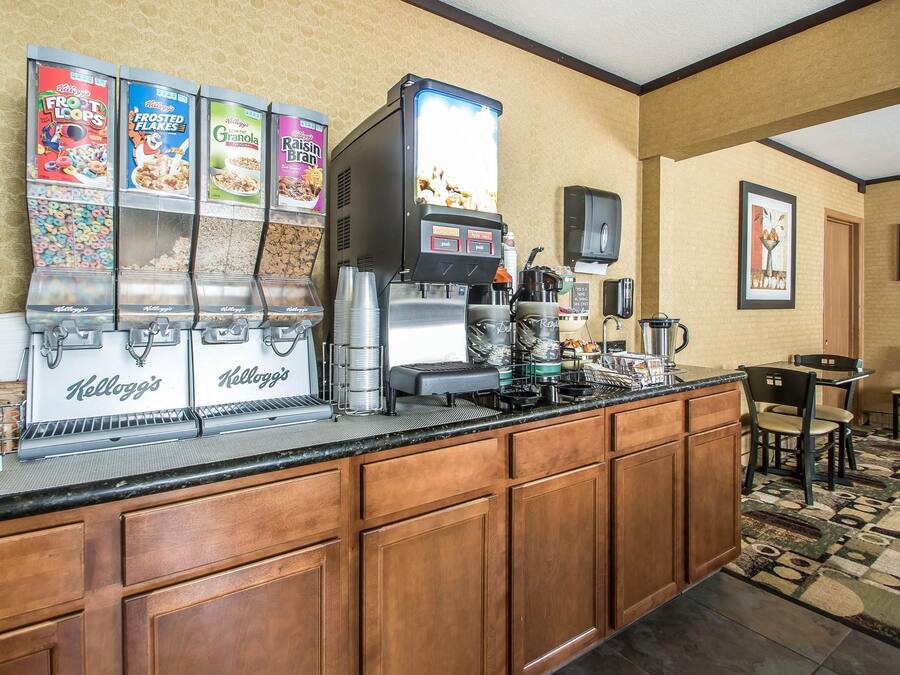 Uma cozinha de hotel com um serviço de café da manhã por conta própria, destacando máquinas dispensadoras de cereais Kellogg's e uma máquina de café.