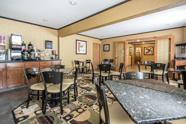 Un comedor de hotel con una estación de café, varias mesas y sillas, y una alfombra estampada.