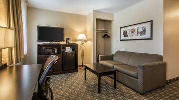 A hotel room with a flat-screen TV, a sofa, a coffee table, a desk, a lamp, a microwave, and a framed picture on the wall.