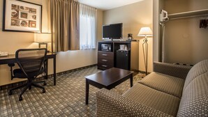 A hotel room with a bed, a desk with a computer, a chair, a TV, a lamp, and a window with curtains. - Quality Inn & Suites Decorah (Decorah)