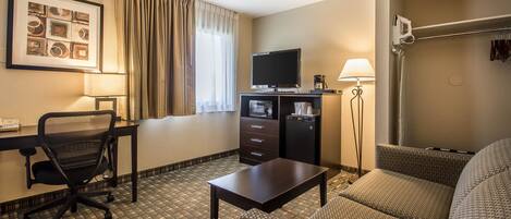 A hotel room with a bed, a desk with a computer, a chair, a TV, a lamp, and a window with curtains.