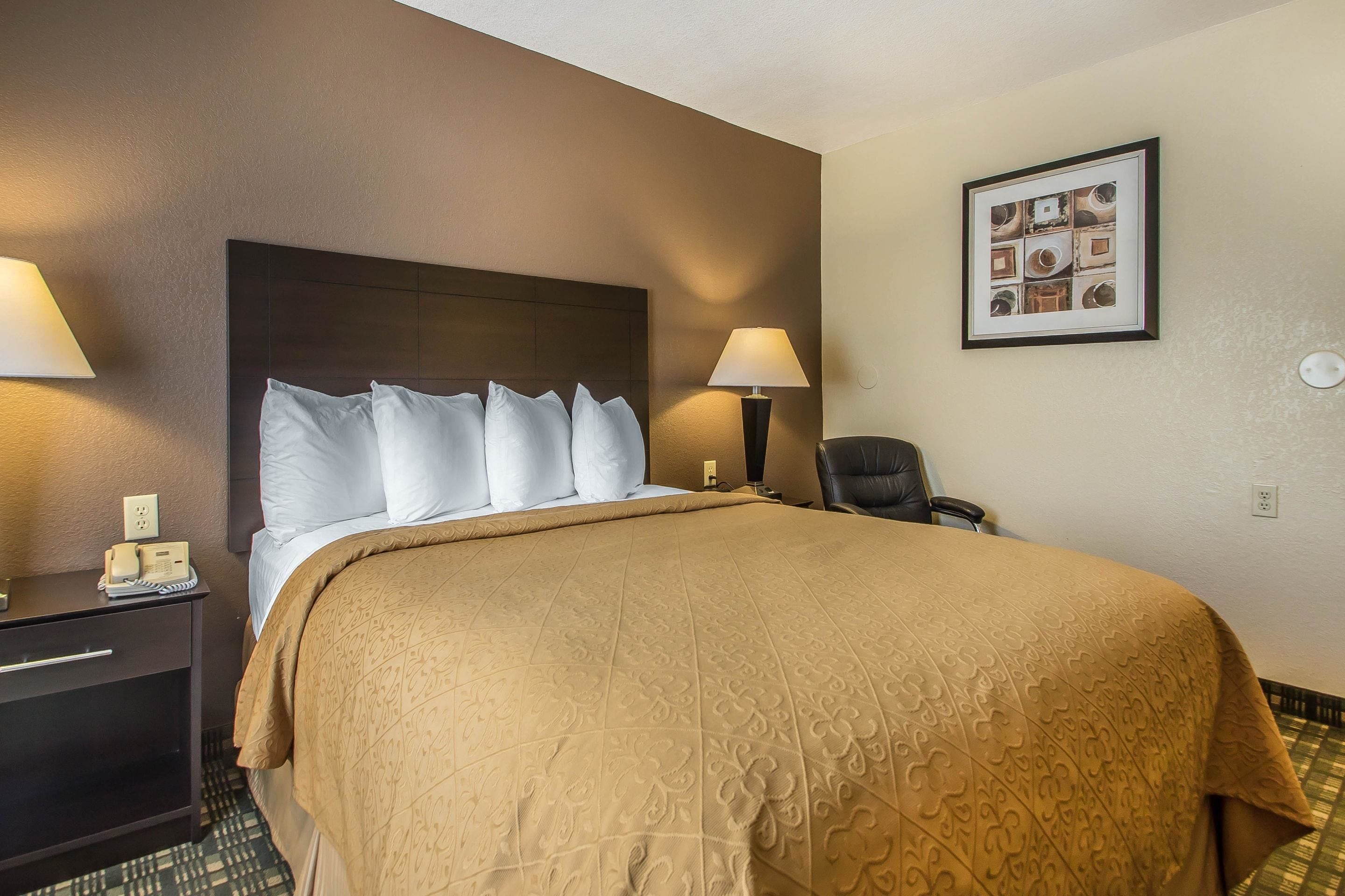 Habitación de hotel con una cama grande, dos lámparas de noche, una silla y un cuadro en la pared.