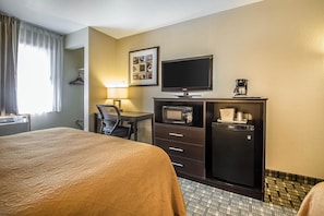 Une chambre d’hôtel équipée d’un lit, d’un bureau avec une chaise, d’une télévision, d’un four à micro-ondes et d’une machine à café.