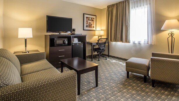 A hotel room with a sofa, a small table, a desk with a chair, a television, and a window with curtains. - Quality Inn & Suites Decorah (Decorah)