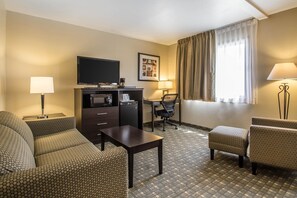 Une chambre d’hôtel avec un canapé, une petite table, un bureau avec une chaise, une télévision et une fenêtre avec des rideaux.