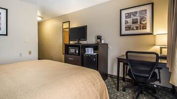 A hotel room with a large bed, a desk with a computer, a television, and a coffee maker.