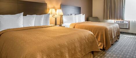 Habitación de hotel con dos camas, cabecera, lámpara, silla, unidad de aire acondicionado y ventana con cortinas.