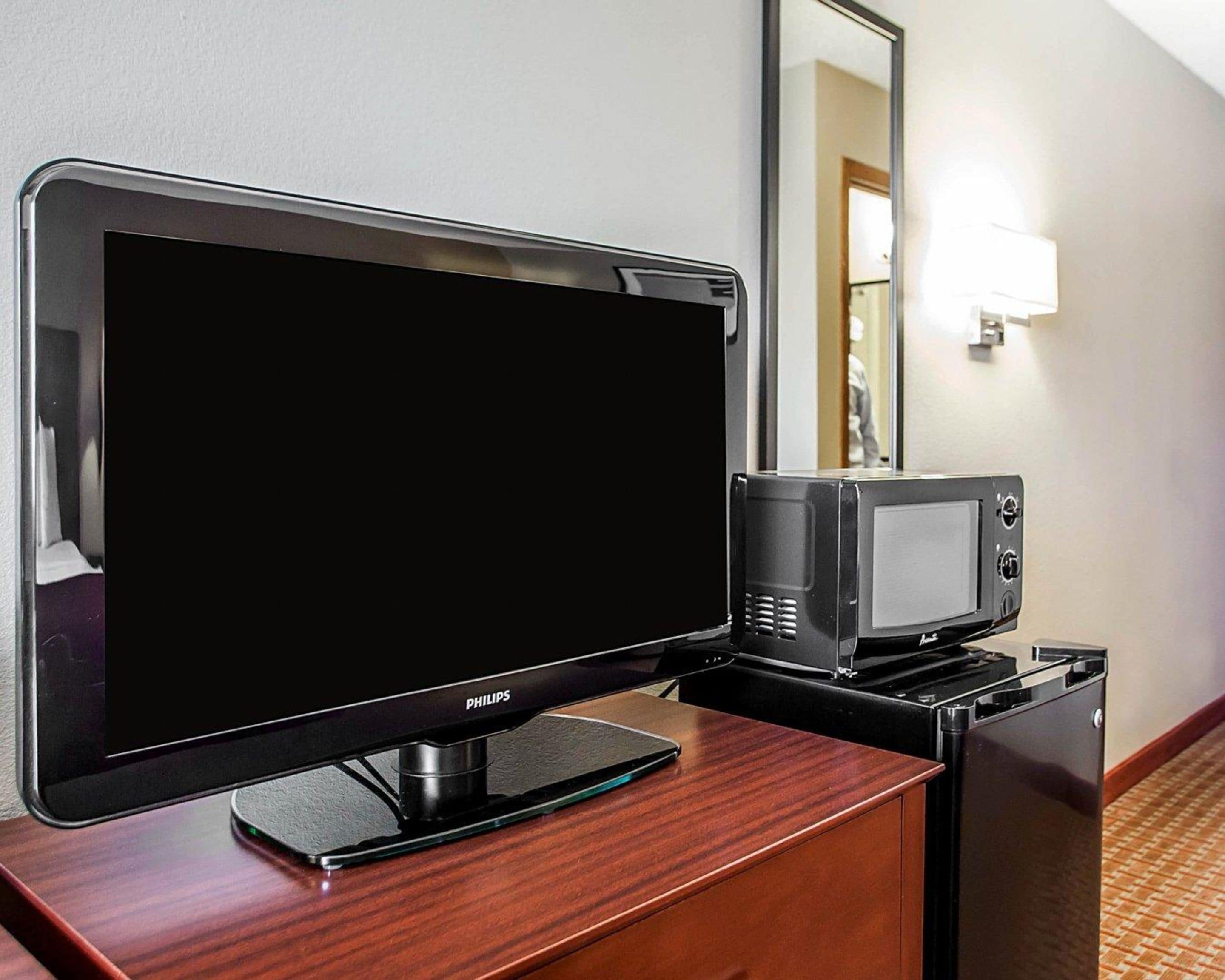 A hotel room with a flat-screen TV and a microwave on a wooden dresser.