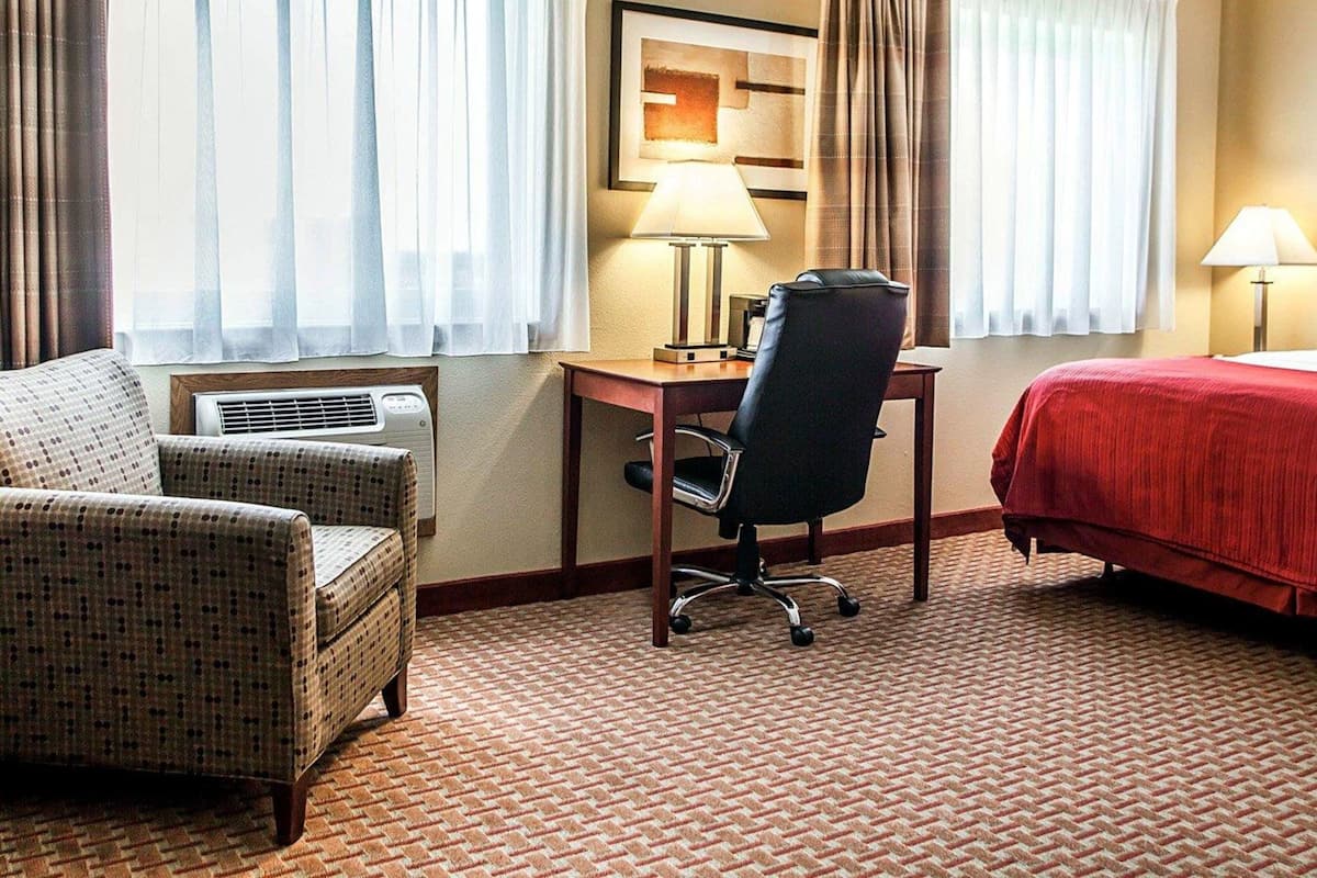 A hotel room with a bed, a desk, a chair, and a window with curtains.