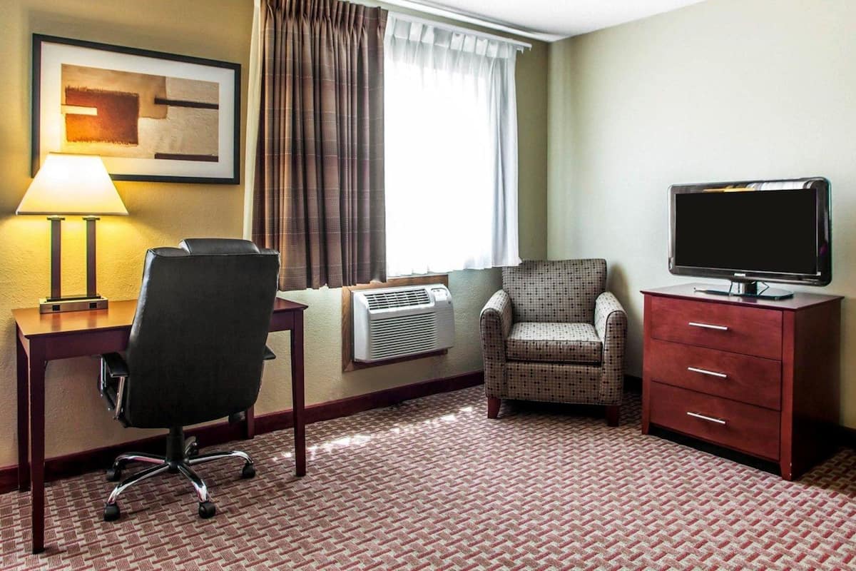 A hotel room with a desk, chair, television, and a red dresser.