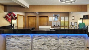 Un hall d'accueil d'hôtel avec un mur en pierre en arrière-plan, une enseigne indiquant « Qualité », des trophées encadrés et un comptoir d'accueil.