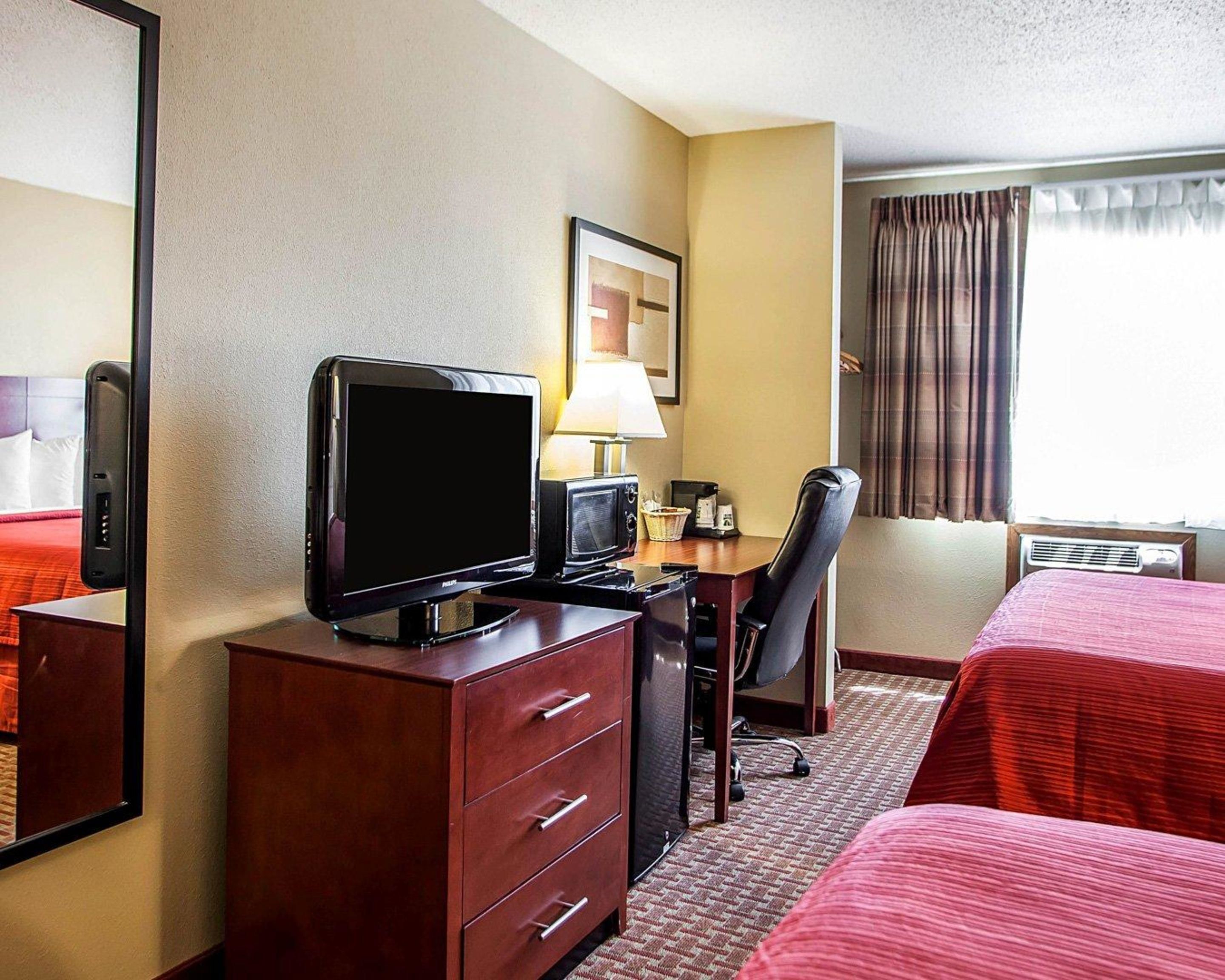 Una habitación de hotel con cama, escritorio, computadora, televisor y lámpara.
