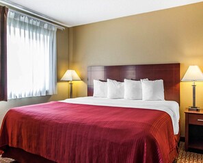 A hotel room with a large bed, two bedside lamps, a wooden headboard, and a window with curtains.