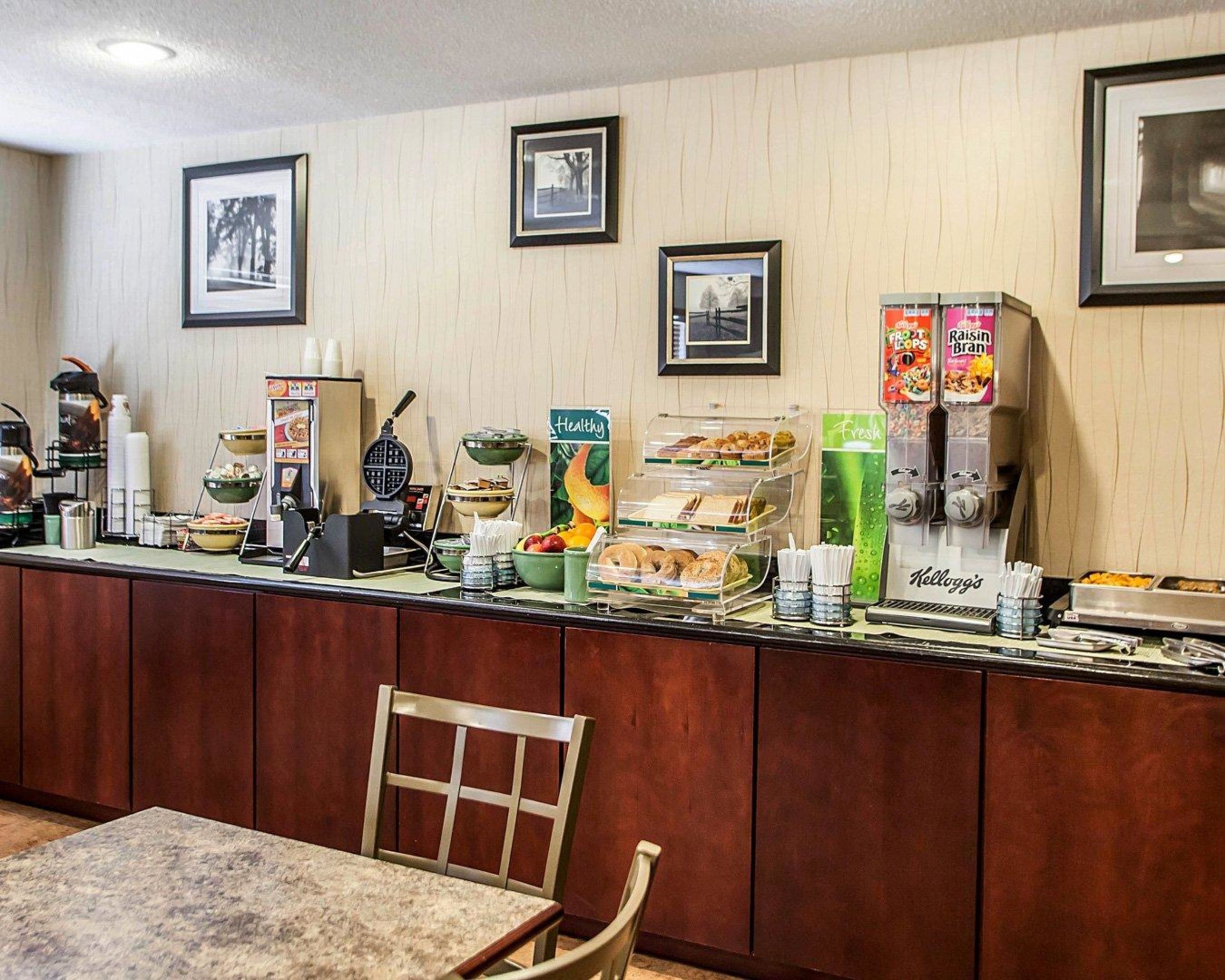 A breakfast bar with various food items and beverages, including a waffle maker, coffee machine, and a refrigerator with fresh produce.