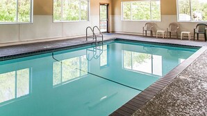 Une piscine intérieure avec des parois en verre transparent, une échelle en métal et plusieurs chaises disposées le long du bord.