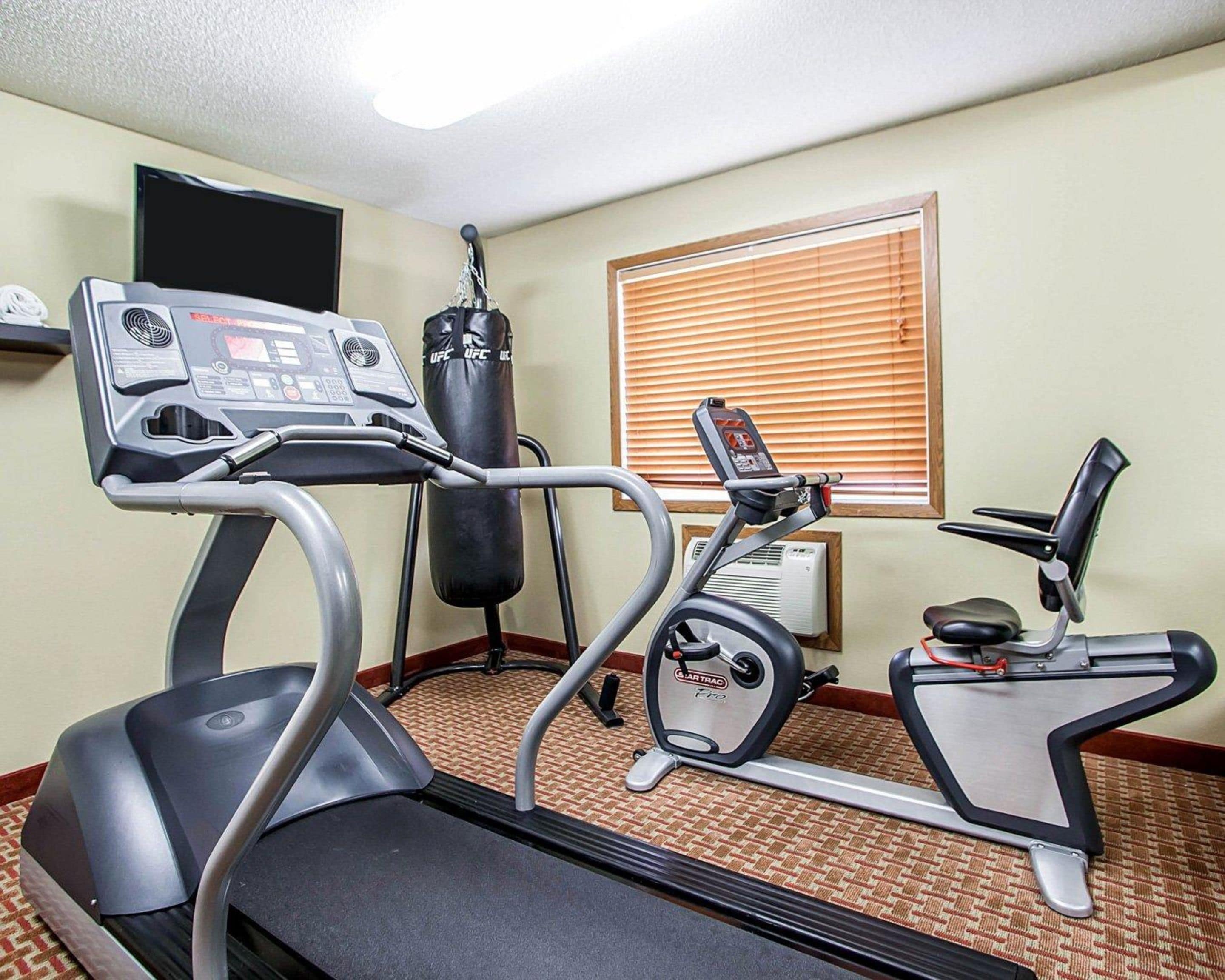 Een hotel fitnessruimte met een loopband, elliptische trainer, bokszak en een aan de muur bevestigde televisie.