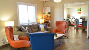 A living room with a sofa, two armchairs, a coffee table, and a dining area with chairs and a table. - Quality Inn & Suites Ankeny - Des Moines (Ankeny)