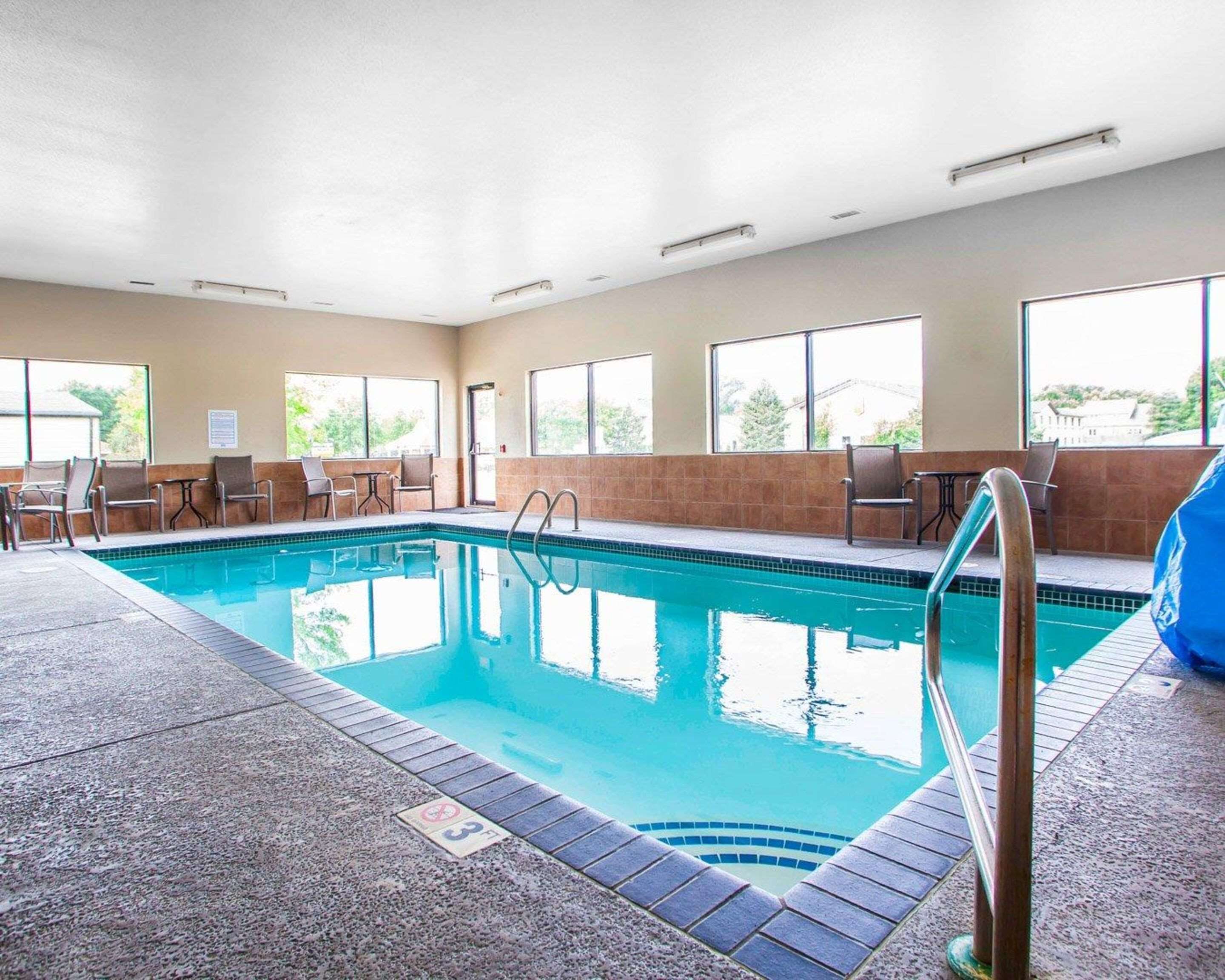 An indoor swimming pool with a tiled deck, lounge chairs, and large windows.