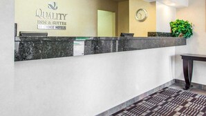 A hotel reception area with a marble counter, a clock, and a sign for Quality Inn & Suites by Choice Hotels. - Quality Inn & Suites Ankeny - Des Moines (Ankeny)