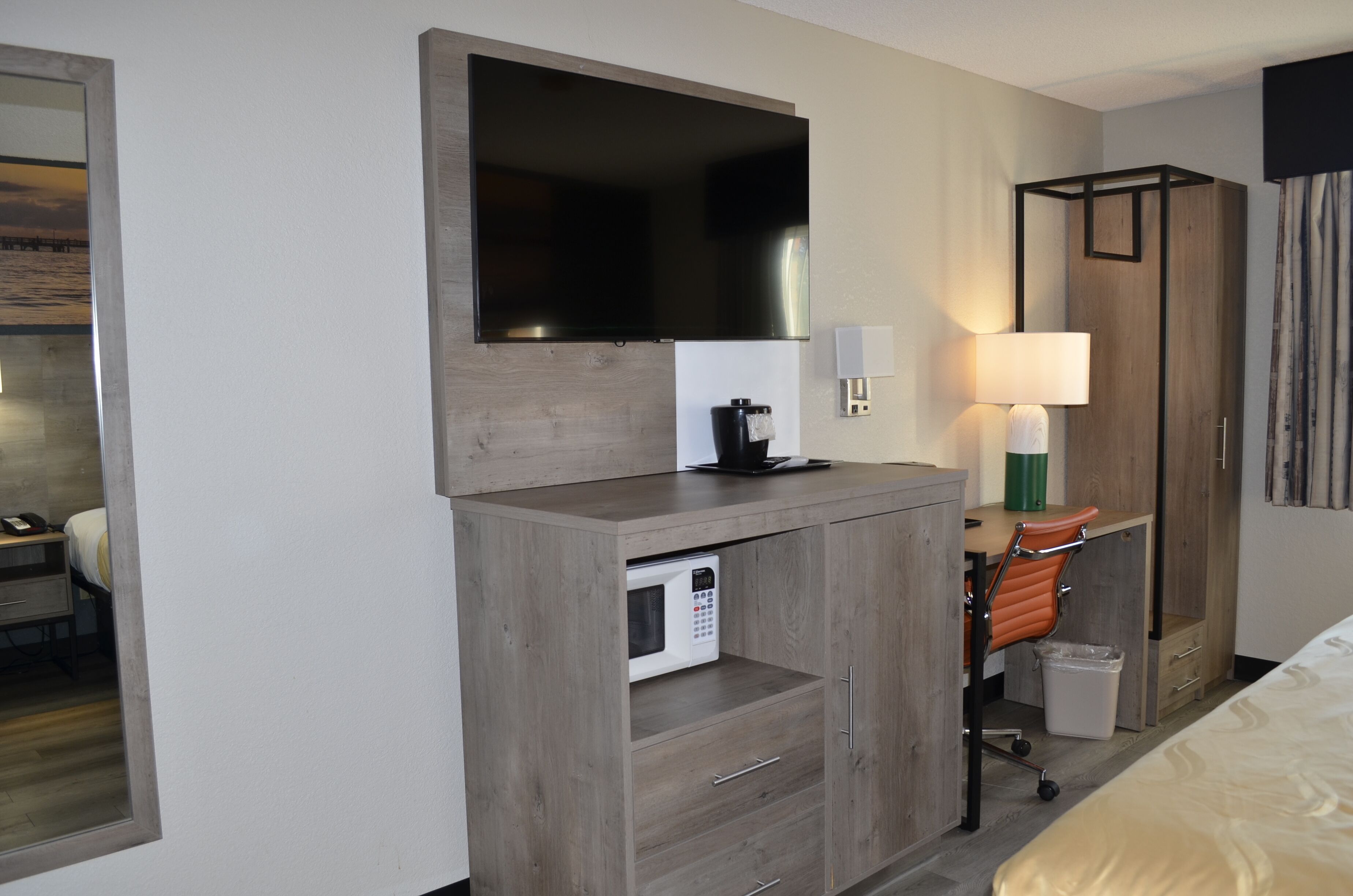 Quarto de hotel com uma grande TV de tela plana presa a um armário de madeira, micro-ondas, escrivaninha com cadeira e cama.
