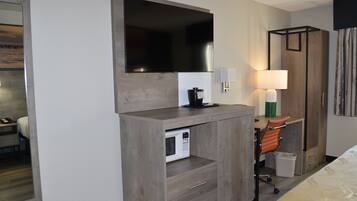 Quarto de hotel com uma grande TV de tela plana presa a um armário de madeira, micro-ondas, escrivaninha com cadeira e cama.