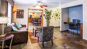 A living room with a sofa, a patterned armchair, a dining area, a kitchen, and a desk with a computer. - Quality Inn & Suites Ankeny - Des Moines (Ankeny)