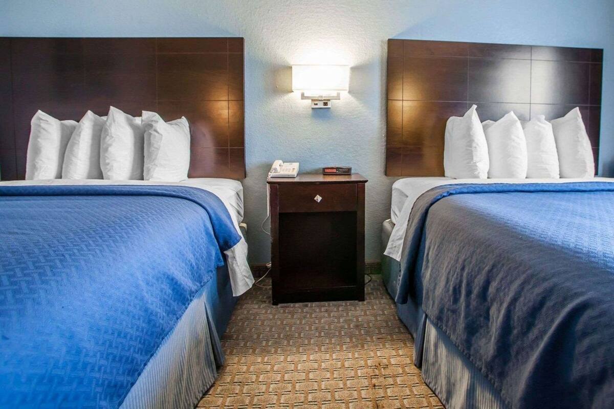 A hotel room with two beds, a nightstand, a wall-mounted light, and a patterned floor.
