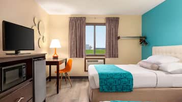 A hotel room with a bed, a desk with a chair, a television, a microwave, and an air conditioning unit.