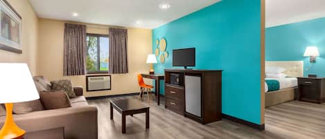 Une chambre d’hôtel avec un mur d’accent de couleur turquoise, un canapé, une télévision, un bureau avec une lampe et un lit avec une tête de lit blanche.