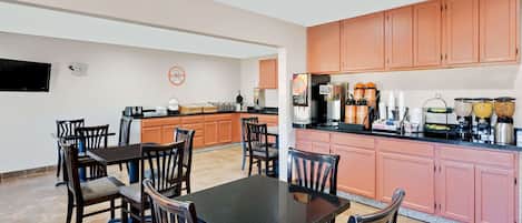 Een moderne keuken met een eethoek, met een zwarte eettafel, houten stoelen en een keukenwerkblad met diverse apparaten en opbergruimte.