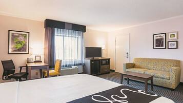 Quarto de hotel com cama, escrivaninha, cadeira, sofá, televisão e porta.