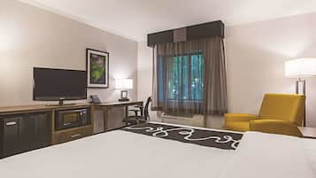 Quarto de hotel com cama, escrivaninha, televisão, cadeira e janela com cortinas.