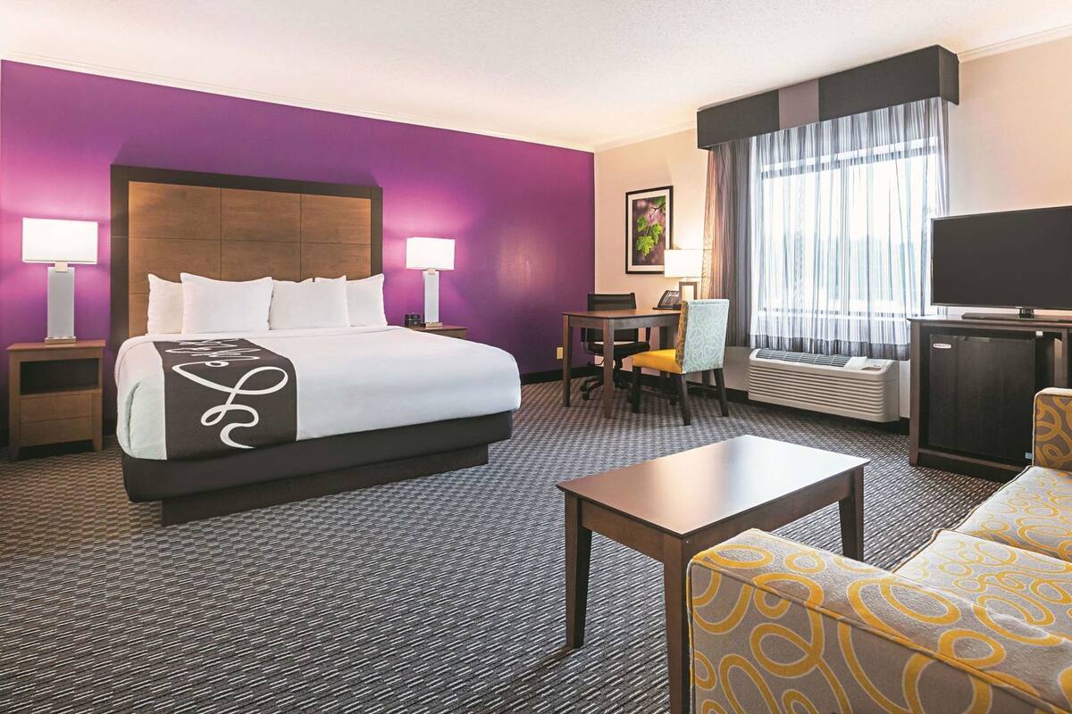 A hotel room with a bed, a desk, a chair, a TV, and a small table.