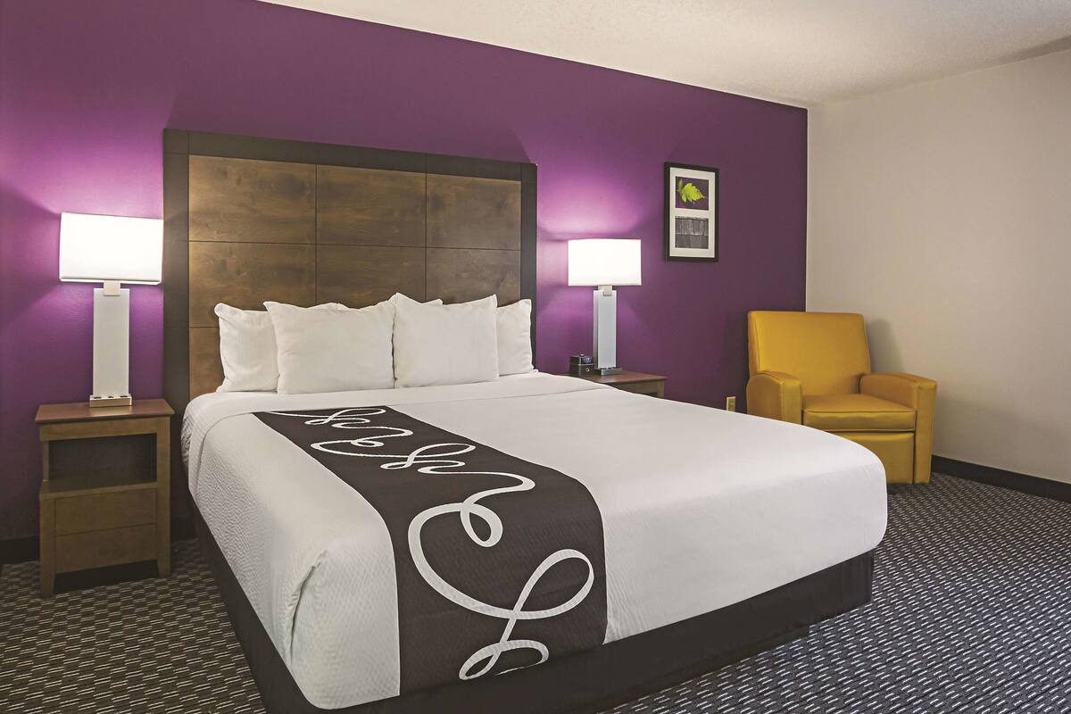 A hotel room with a large bed, two bedside lamps, a chair, and a headboard.
