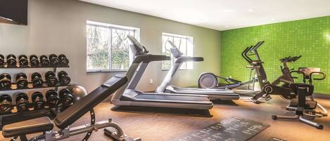 A gym with treadmills, an elliptical, and a spinning bike. There are dumbbells on a rack and a yoga mat on the floor.