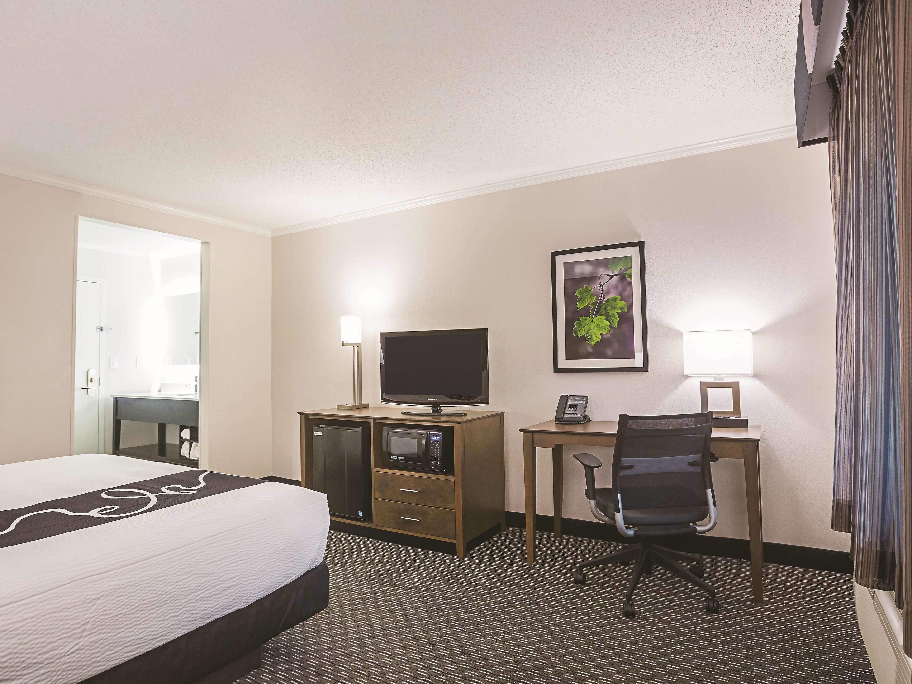 Una habitación de hotel con una cama, un escritorio con computadora, televisor y teléfono.