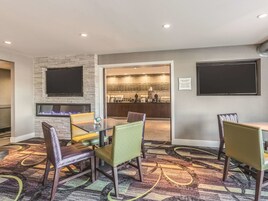 A hotel room with a fireplace, a dining area with chairs, a kitchen area, and a flat-screen TV mounted on the wall.