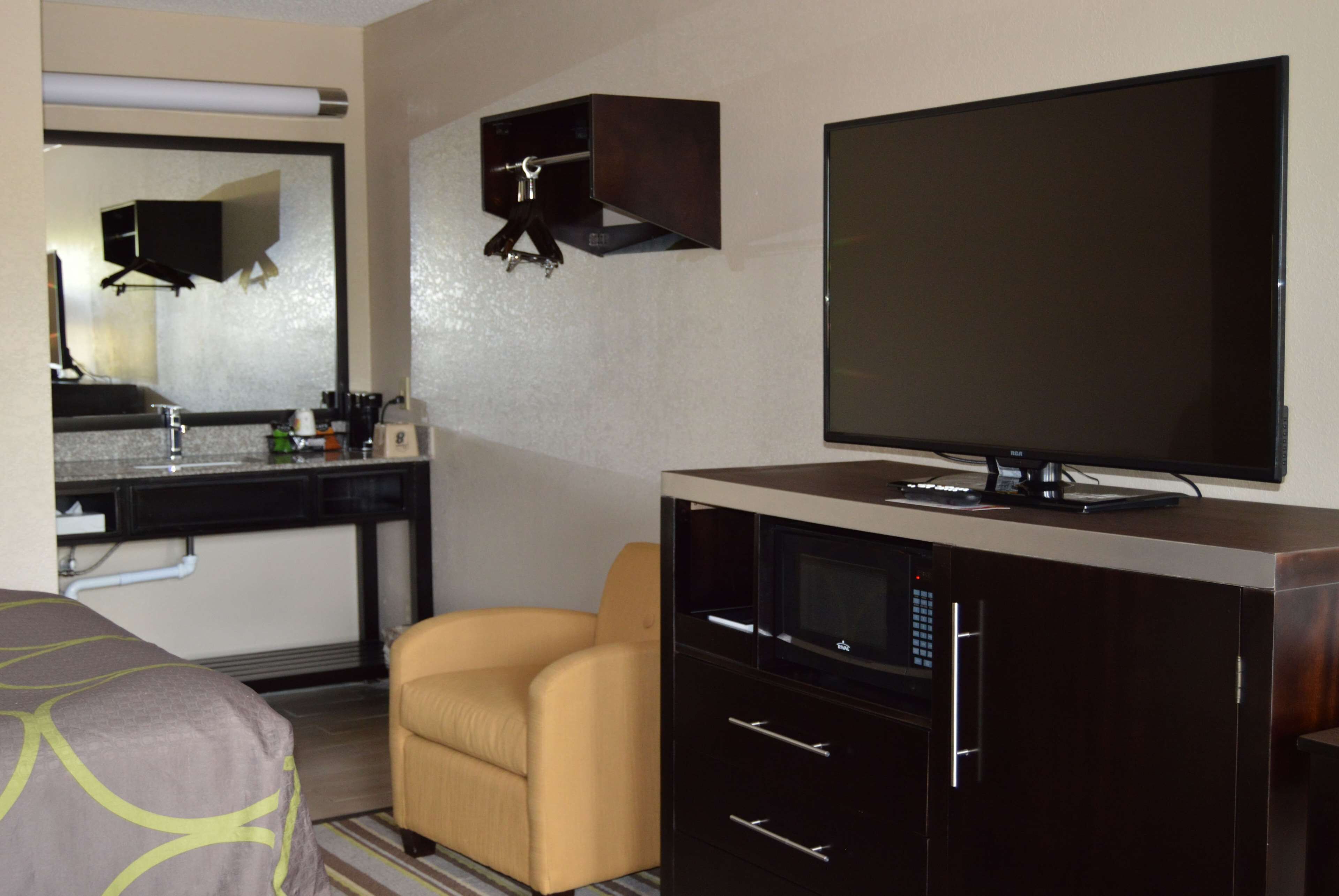 A hotel room with a bed, a television, a desk with a computer, a chair, and a small cabinet.