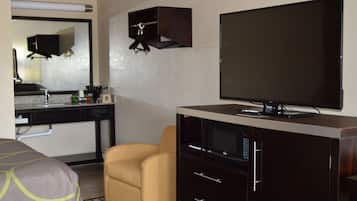 A hotel room with a bed, a television, a desk with a computer, a chair, and a small cabinet.