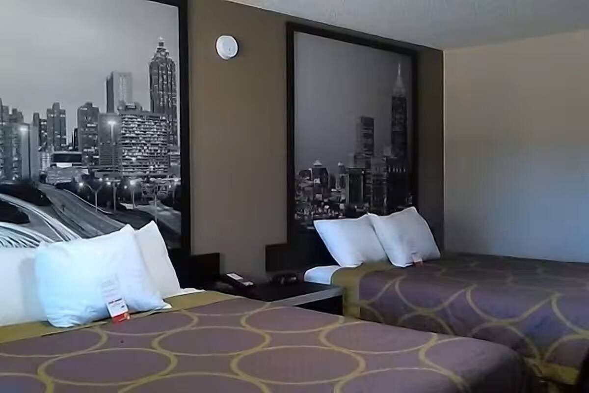 A hotel room with two beds, a cityscape mural on the wall, and a clock.