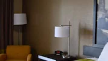A hotel room with a bed, a nightstand, a lamp, a chair, and a wall with a painting.