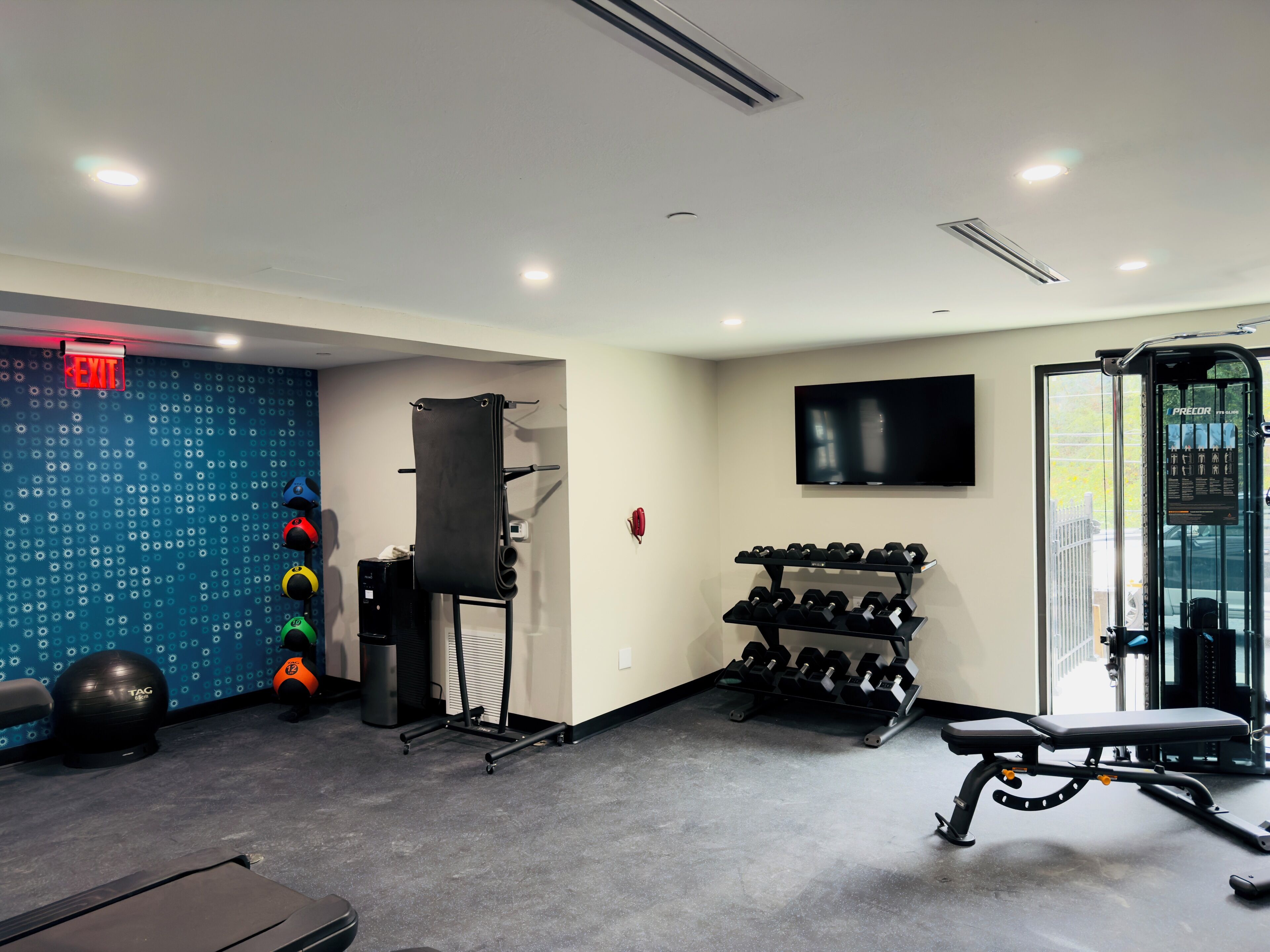 A gym with exercise equipment, a wall-mounted TV, and a blue patterned wall.
