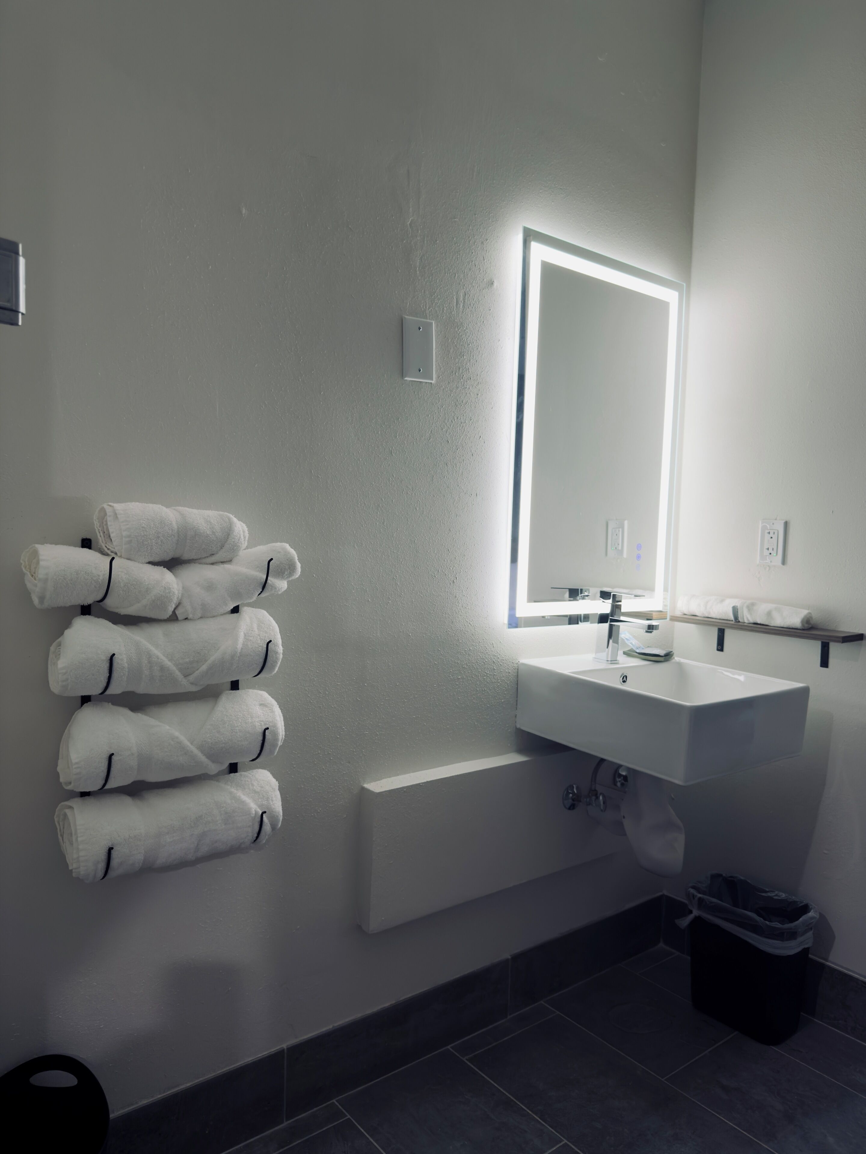 Un baño moderno con un lavamanos blanco, un espejo y un perchero con toallas dobladas con cuidado.