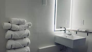 Un baño moderno con un lavamanos blanco, un espejo y un perchero con toallas dobladas con cuidado.