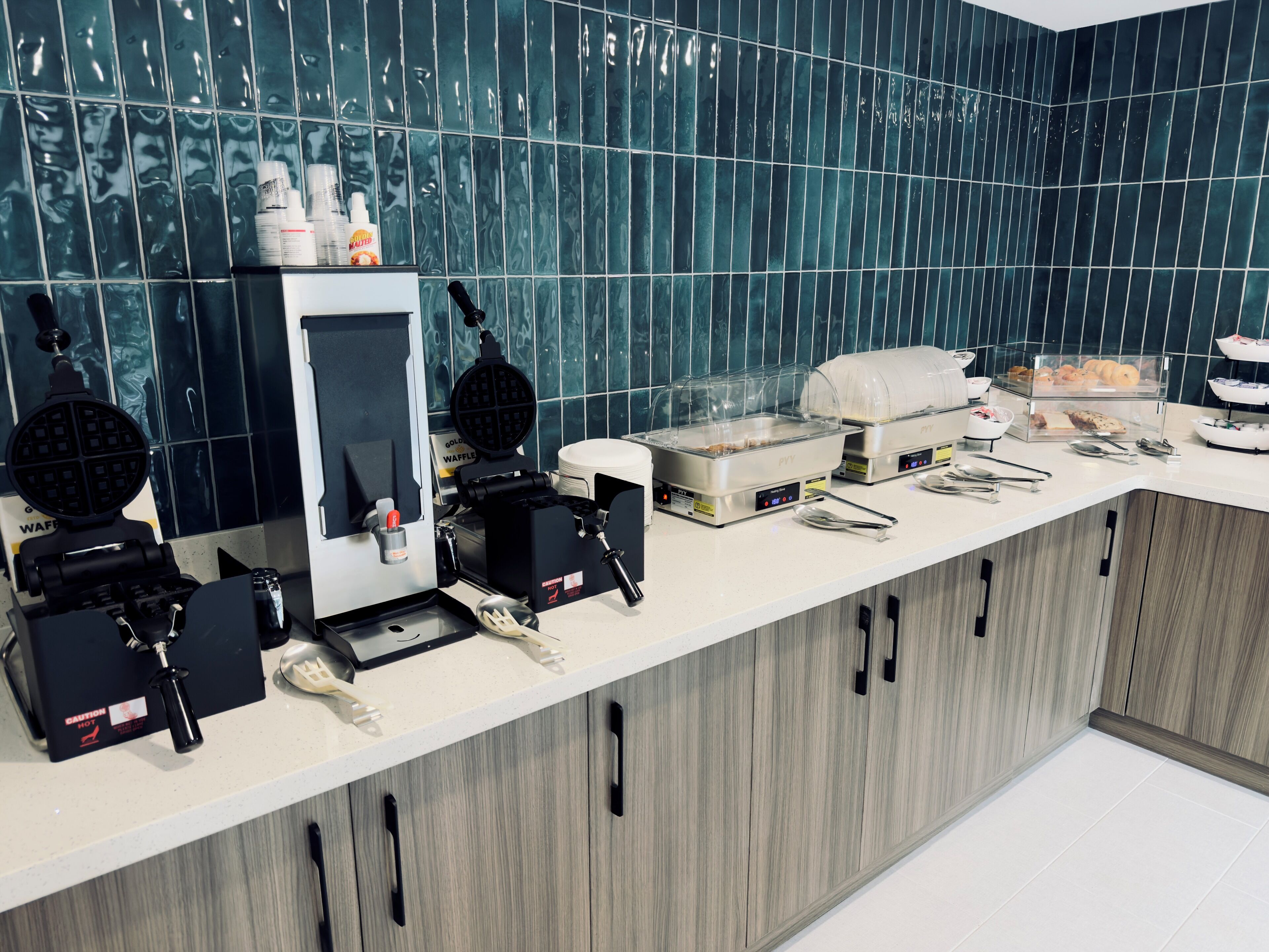 A breakfast bar with waffle makers, a coffee machine, and a variety of food items.