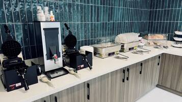 A breakfast bar with waffle makers, a coffee machine, and a variety of food items.