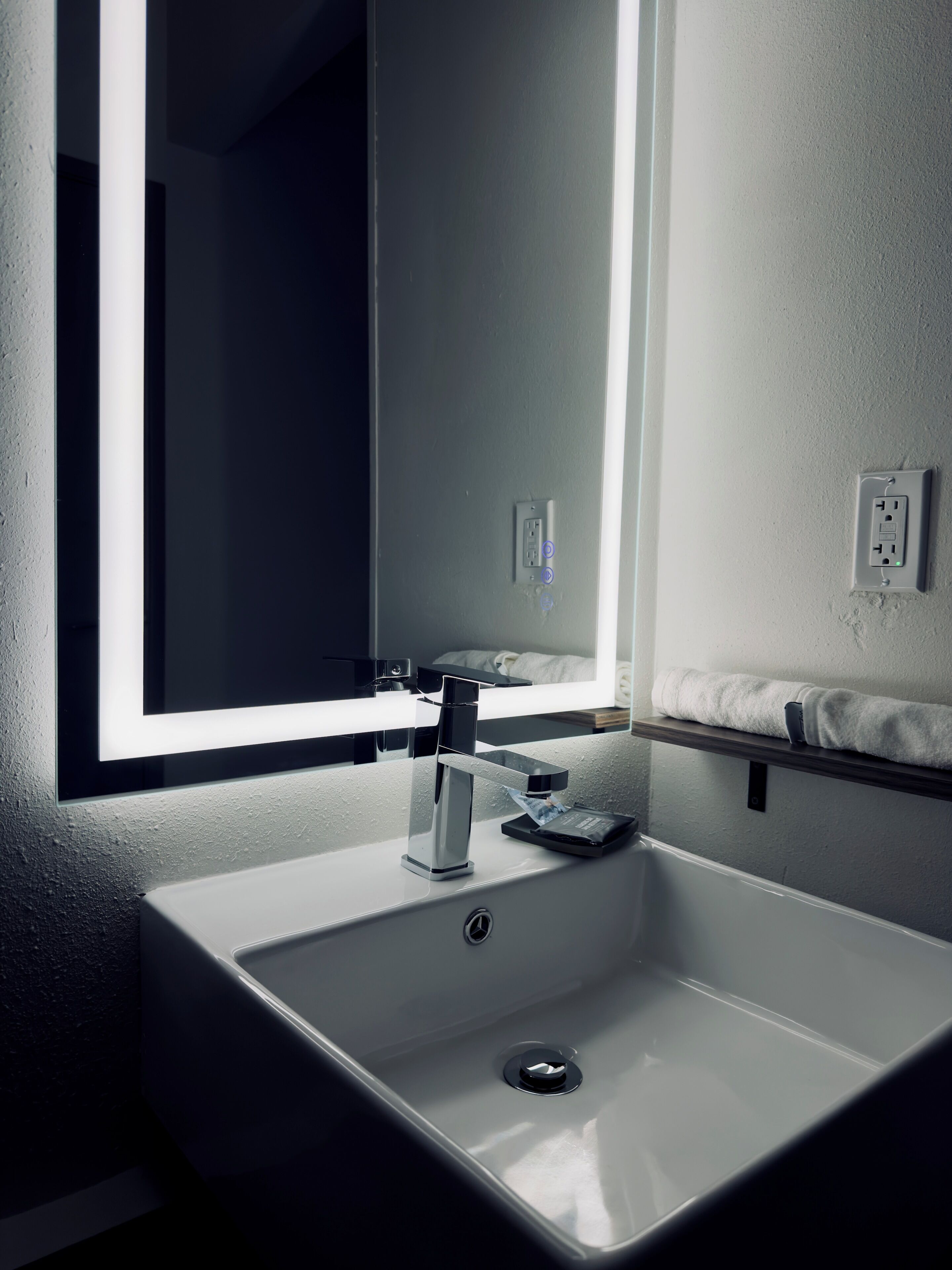 Un baño moderno con un lavamanos blanco, un espejo y un perchero para toallas.