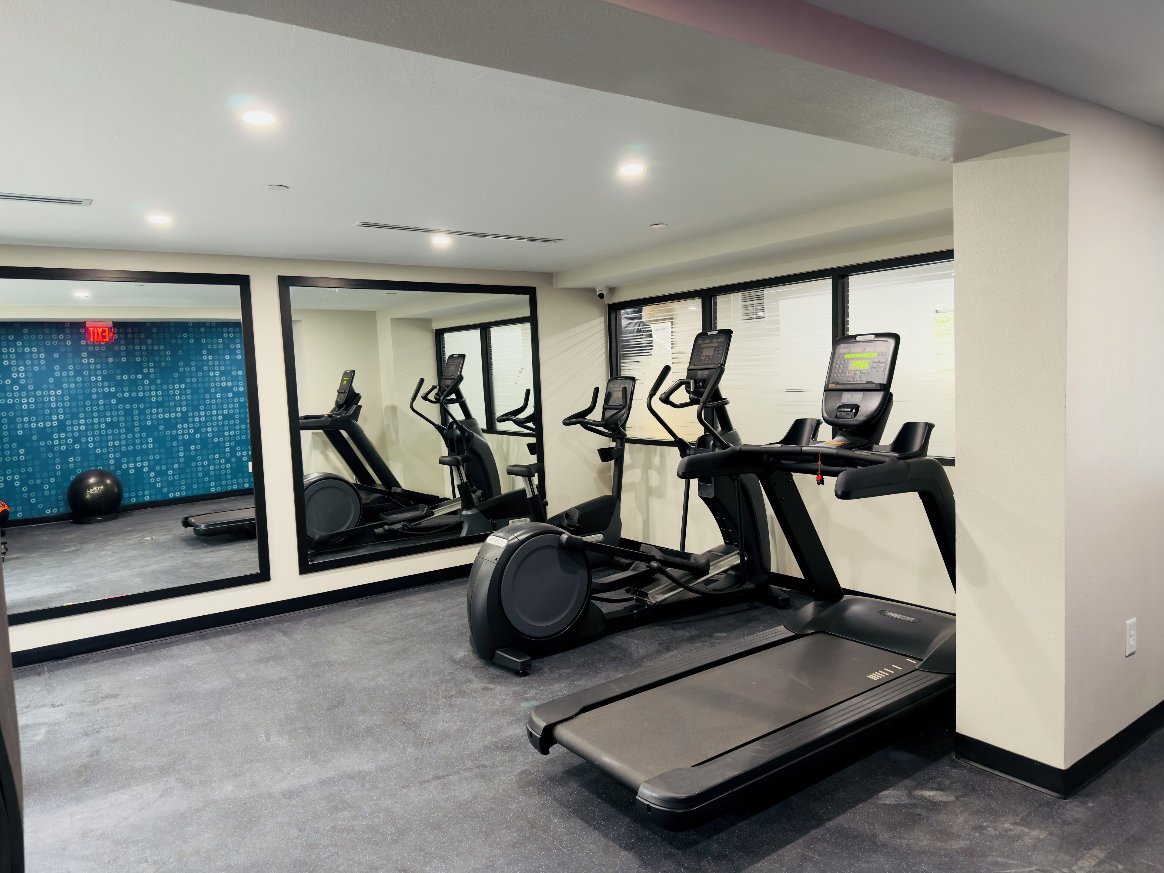 A gym with exercise equipment, including treadmills and an elliptical, and a mirrored wall.